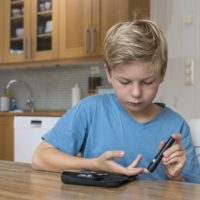 Child with diabetes measuring glucose or blood level in a kitchen